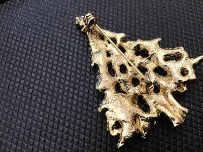 Sale Photo Thumbnail #89: A vintage gold-tone Christmas tree brooch featuring textured branch details, topped with a clear rhinestone star, and accented with red, blue, and green rhinestones. The pin back features a rollover safety clasp mechanism. Appears in good pre-owned condit