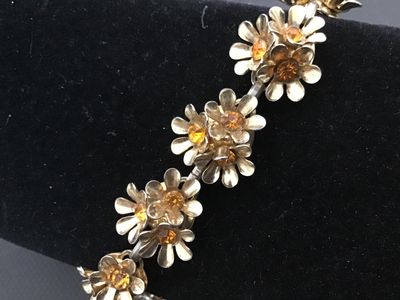 Sale Photo Thumbnail #173: Vintage Coro gold-tone bracelet featuring multi-petal floral links set with amber or topaz-colored rhinestones. Includes a fold-over clasp marked "Coro". Light vintage wear consistent with age, overall good condition with all stones present.
