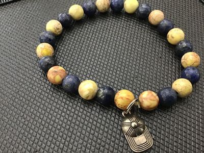 Sale Photo Thumbnail #116: Natural stone round beaded stretch bracelet featuring alternating blue sodalite/lapis and yellow-earth tone jasper or marble beads. Includes a silvertone metal baseball cap charm attached to a split ring. Measures approximately 7 to 7.5 inches around on a
