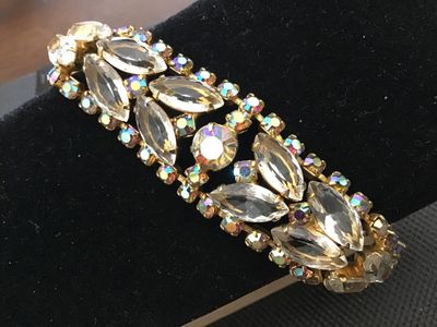 Sale Photo Thumbnail #53: A vintage gold-tone costume jewelry bracelet featuring clear marquise-cut rhinestones flanked by iridescent aurora borealis accent crystals. Features a fold-over clasp closure. Measures approximately 7 inches long. Good vintage condition with light surfac