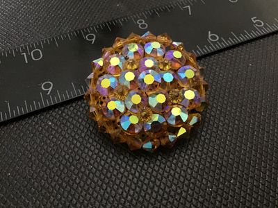 Sale Photo Thumbnail #236: Vintage round domed cluster brooch set with iridescent aurora borealis rhinestones and amber/topaz-colored faceted crystal beads. Features a textured silver-tone backing with a locking pin clasp. Measures approximately 1.5 inches in diameter. In good vint