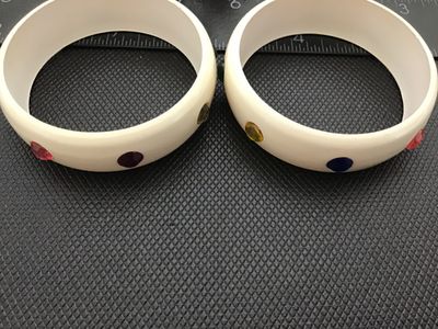 Sale Photo Thumbnail #5: Pair of cream/off-white plastic or lucite thick bangle bracelets studded with round faceted multi-colored rhinestones (red, blue, green, purple, yellow). Each bangle measures approximately 2.5 inches in inner diameter. Both bracelets are in good vintage c