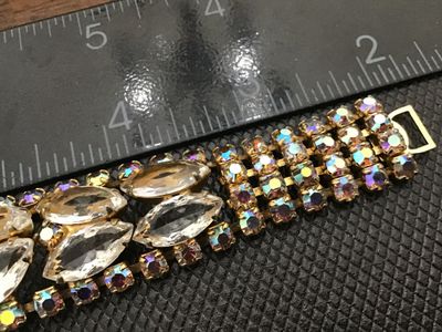 Sale Photo Thumbnail #56: A vintage gold-tone costume jewelry bracelet featuring clear marquise-cut rhinestones flanked by iridescent aurora borealis accent crystals. Features a fold-over clasp closure. Measures approximately 7 inches long. Good vintage condition with light surfac
