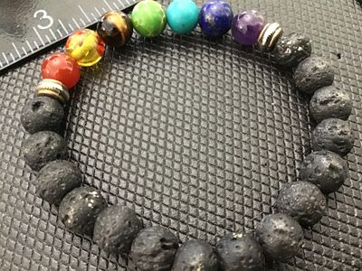 Sale Photo Thumbnail #101: Stretch beaded bracelet featuring black porous lava rock/lava stone beads and seven multi-colored gemstone-style chakra accent beads separated by small metal spacer beads. Appears to be in good pre-owned condition with light wear.