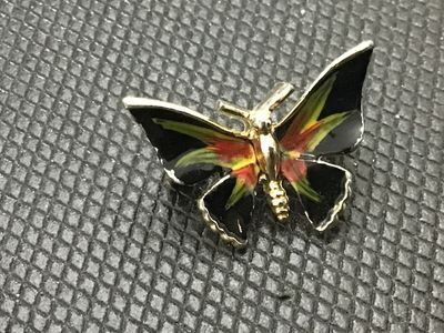 Sale Photo Thumbnail #216: A gold-tone butterfly pin brooch featuring black, green, and red enamel detailing on the wings. Standard rollover safety clasp on the back. Shows light surface wear consistent with age, but overall in good pre-owned condition.