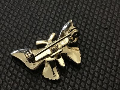 Sale Photo Thumbnail #217: A gold-tone butterfly pin brooch featuring black, green, and red enamel detailing on the wings. Standard rollover safety clasp on the back. Shows light surface wear consistent with age, but overall in good pre-owned condition.