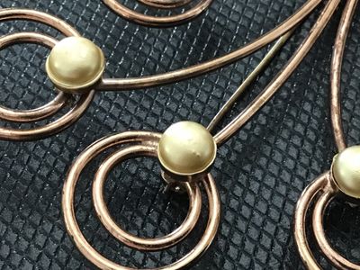 Sale Photo Thumbnail #122: A vintage wirework brooch designed as a floral spray or bouquet, tied with a ribbon bow. Crafted in a rose gold tone metal with swirling wire details topped with Cream-colored faux pearl accents. Measures approximately 2.5 inches wide. Shows light age-app