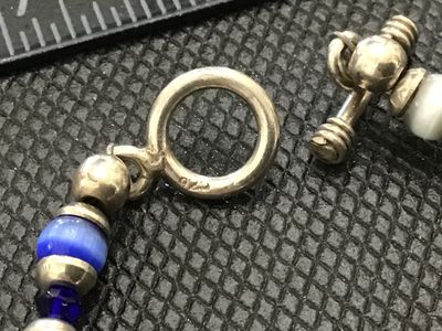 Sale Photo Thumbnail #212: A beaded toggle-clasp bracelet featuring colorful cat's eye synthetic or glass beads alternating with faceted crystal spacers and silver-tone accents. Includes an oval central charm with an engraved script monogram ("MJL"). The toggle ring is stamped "925