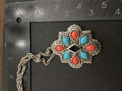 Sale Photo Thumbnail #229: A vintage Avon silver-tone convertible pendant brooch necklace featuring a Southwestern style starburst medallion set with faux turquoise, coral-colored, and black resin stones. The versatile piece functions as both a pendant on a twisted rope chain and a