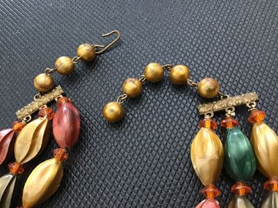 Sale Photo Thumbnail #188: A vintage 3-strand beaded necklace featuring swirl/leaf-molded plastic beads in earth tones (green, gold, bronze, terracotta/coral), accented with faceted crystal and amber spacer beads. Includes decorative metal bar connectors and a hook-and-tail clasp e