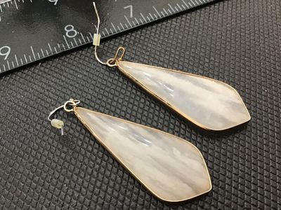 Sale Photo Thumbnail #138: Pair of gold-tone metal dangle drop earrings featuring elongated teardrop-style pendants with semi-translucent white marbled or swirled stone/acrylic inlay. Ear wires include plastic backs. Total length is approximately 2.5 inches. In good pre-owned condi