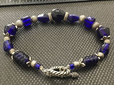 Sale Photo Thumbnail #145: Beaded bracelet featuring vibrant cobalt blue art glass beads in various shapes and textures, interspersed with ornate silver-tone spacer beads, bead caps, and a decorative rope-style toggle clasp. Measures approximately 7 to 7.5 inches long. In good cond
