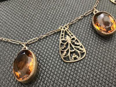 Sale Photo Thumbnail #84: Vintage or antique-style choker necklace featuring intricate metal filigree teardrop charms alternating with bezel-set faceted oval amber/topaz-colored glass stones. Connected on a paperclip-link chain with a hook clasp. Metal shows light tarnishing and p