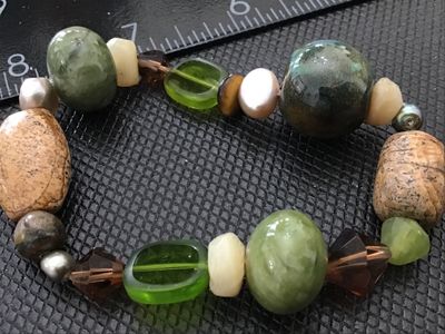 Sale Photo Thumbnail #144: An artisan beaded stretch bracelet featuring an eclectic mix of earth-toned elements, including green jade-like stones, picture jasper, iridescent pearls, faceted glass, and glazed ceramic beads. In good pre-owned condition with no visible damage.