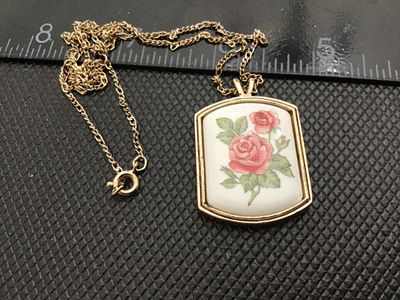Sale Photo Thumbnail #51: Vintage Avon gold-tone necklace featuring a rectangular pendant with a raised ceramic or porcelain inset depicting pink roses with green leaves. Marked '© AVON' on the textured reverse side. Includes a gold-tone fine link chain with a spring-ring clasp. 