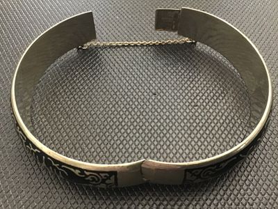 Sale Photo Thumbnail #65: A vintage Siam niello style hinged bangle bracelet featuring black enamel/niello inlay with etched architectural and decorative motifs around the exterior. Equipped with a box tab closure and attached safety chain. Marked 'WHITE ' on the interior. Shows l