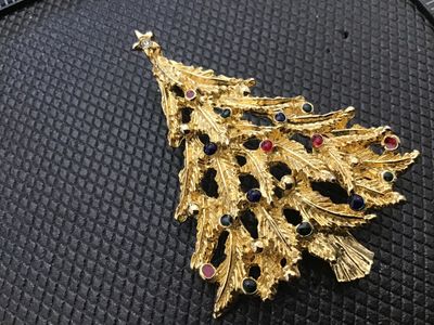 Sale Photo Thumbnail #88: A vintage gold-tone Christmas tree brooch featuring textured branch details, topped with a clear rhinestone star, and accented with red, blue, and green rhinestones. The pin back features a rollover safety clasp mechanism. Appears in good pre-owned condit