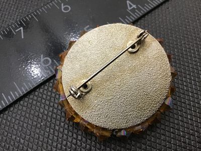 Sale Photo Thumbnail #238: Vintage round domed cluster brooch set with iridescent aurora borealis rhinestones and amber/topaz-colored faceted crystal beads. Features a textured silver-tone backing with a locking pin clasp. Measures approximately 1.5 inches in diameter. In good vint