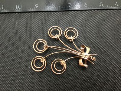 Sale Photo Thumbnail #121: A vintage wirework brooch designed as a floral spray or bouquet, tied with a ribbon bow. Crafted in a rose gold tone metal with swirling wire details topped with Cream-colored faux pearl accents. Measures approximately 2.5 inches wide. Shows light age-app