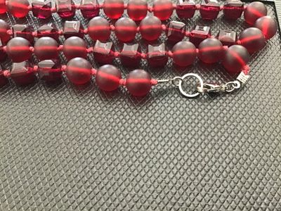 Sale Photo Thumbnail #29: A long single-strand necklace featuring alternating deep red frosted round glass beads and faceted geometric glass beads, hand-knotted on red cord. Finished with a silver-tone lobster clasp closure. Measures approximately 24 to 26 inches in total length. 