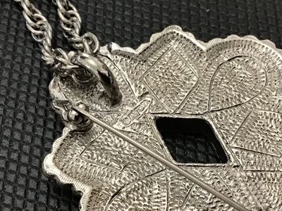 Sale Photo Thumbnail #230: A vintage Avon silver-tone convertible pendant brooch necklace featuring a Southwestern style starburst medallion set with faux turquoise, coral-colored, and black resin stones. The versatile piece functions as both a pendant on a twisted rope chain and a