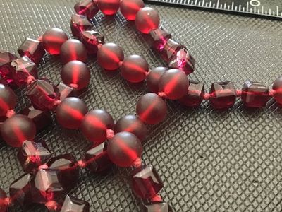 Sale Photo Thumbnail #26: A long single-strand necklace featuring alternating deep red frosted round glass beads and faceted geometric glass beads, hand-knotted on red cord. Finished with a silver-tone lobster clasp closure. Measures approximately 24 to 26 inches in total length. 