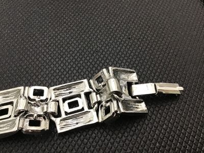 Sale Photo Thumbnail #180: A vintage silver-tone wide link panel bracelet featuring a textured bark-like finish and geometric rectangular cut-out links. Features a fold-over clasp closure. Measures approximately 7.5 inches long. Shows minor vintage wear consistent with age, but ove