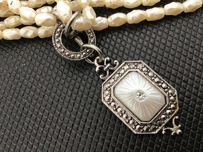 Sale Photo Thumbnail #13: Avon costume jewelry necklace featuring multi-strand white faux rice pearls, a toggle clasp, and an Art Deco style silvertone pendant set with mother of pearl style face and clear rhinestone accent. Stamped ©AVON on the back of the pendant. Measures appr