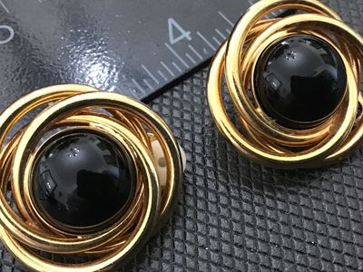 Sale Photo Thumbnail #78: Pair of vintage gold-tone clip-on earrings featuring a multi-ring swirl design centered with a glossy black cabochon stone. The clip backs are functional and include soft comfort pads. Measure approximately 1 inch in diameter. In good condition with minim