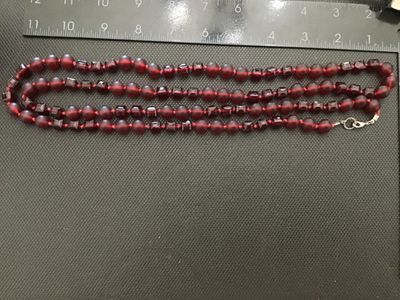 Sale Photo Thumbnail #30: A long single-strand necklace featuring alternating deep red frosted round glass beads and faceted geometric glass beads, hand-knotted on red cord. Finished with a silver-tone lobster clasp closure. Measures approximately 24 to 26 inches in total length. 