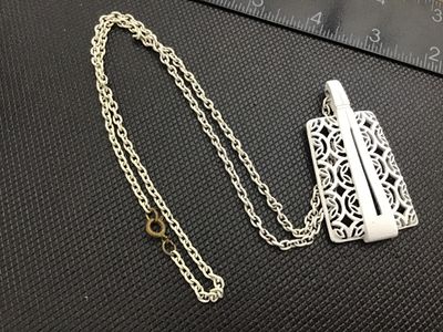 Sale Photo Thumbnail #93: A vintage mid-century style white enamel pendant necklace featuring an openwork, filigree geometric lattice pattern with a sleek modern overlay accent. Suspended from a matching white enamelled link chain with a gold-tone spring ring clasp. 

- Pendant Di