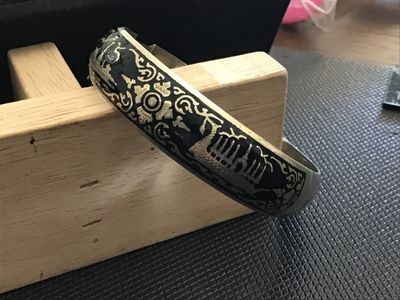 Sale Photo Thumbnail #63: A vintage Siam niello style hinged bangle bracelet featuring black enamel/niello inlay with etched architectural and decorative motifs around the exterior. Equipped with a box tab closure and attached safety chain. Marked 'WHITE ' on the interior. Shows l