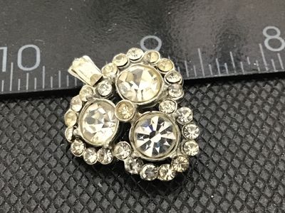Sale Photo Thumbnail #152: Small vintage silver-tone rhinestone brooch shaped like a shamrock or clover with a small stem. Set with three larger round chaton rhinestones, surrounded by halo accents and a baguette stone on the stem. Back features a pin mechanism. Shows light surface