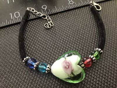 Sale Photo Thumbnail #140: Fashion bracelet featuring a central glass heart charm with encased floral/rose detail, flanked by colorful glass beads and silver-tone spacer accents. Set on a black suede or cord strap with an adjustable chain extender and lobster claw clasp. Good pre-o