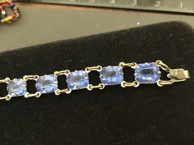 Sale Photo Thumbnail #206: Vintage costume jewelry link bracelet featuring emerald-cut light blue glass stones set in open-backed claw prongs. Includes a decorative filigree push-in box clasp with safety tongue. Measures approximately 7.25 inches in overall length. Metal shows surf