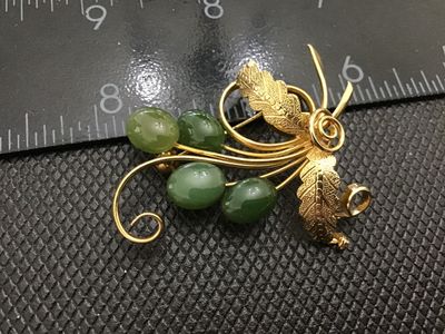 Sale Photo Thumbnail #234: A vintage gold-tone wire-work brooch featuring a leaf and scroll spray design accented with four oval cabochon green stone or glass beads resembling jade. Features textured leaves and a standard pin back clasp. Measures approximately 2 inches long. Good v