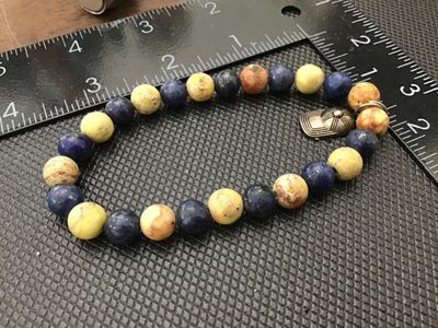 Sale Photo Thumbnail #115: Natural stone round beaded stretch bracelet featuring alternating blue sodalite/lapis and yellow-earth tone jasper or marble beads. Includes a silvertone metal baseball cap charm attached to a split ring. Measures approximately 7 to 7.5 inches around on a