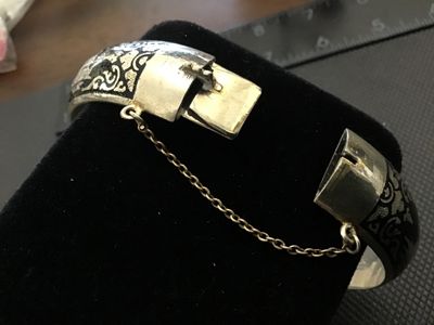 Sale Photo Thumbnail #59: A vintage Siam niello style hinged bangle bracelet featuring black enamel/niello inlay with etched architectural and decorative motifs around the exterior. Equipped with a box tab closure and attached safety chain. Marked 'WHITE ' on the interior. Shows l