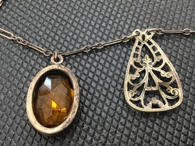 Sale Photo Thumbnail #86: Vintage or antique-style choker necklace featuring intricate metal filigree teardrop charms alternating with bezel-set faceted oval amber/topaz-colored glass stones. Connected on a paperclip-link chain with a hook clasp. Metal shows light tarnishing and p