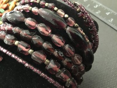 Sale Photo Thumbnail #169: Multi-strand memory wire wrap bracelet featuring an assortment of purple and plum glass beads in faceted, oval, and seed bead shapes with spacer accents. Flexible cuff design easily adjusts to fit most wrists. In good pre-owned condition with minor signs 