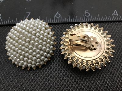 Sale Photo Thumbnail #107: Pair of vintage round clip-on earrings featuring clustered white faux pearl beads in a domed pattern. Set in a gold-tone filigree metal backing. Each earring measures approximately 1.25 inches in diameter. Good vintage condition with light, age-appropriat