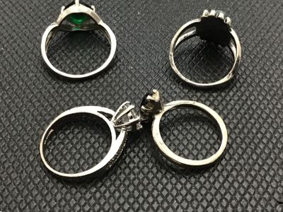 Sale Photo Thumbnail #193: Collection of four silver-toned costume rings featuring various stone designs, including a clear cz-style solitaire with accent stones, a green stone in a bypass-style band, a turquoise-colored cabochon with detailed border, and a black marquise-cut stone