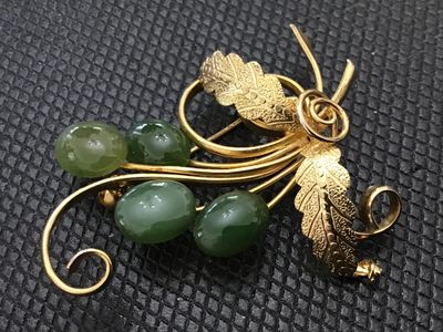 Sale Photo Thumbnail #232: A vintage gold-tone wire-work brooch featuring a leaf and scroll spray design accented with four oval cabochon green stone or glass beads resembling jade. Features textured leaves and a standard pin back clasp. Measures approximately 2 inches long. Good v