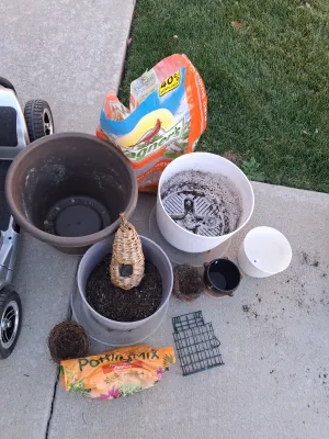 Sale Photo Thumbnail #117: Assorted lawn and garden supply lot including WAGNER'S Songbird Supreme Wild Bird Food, potting mix, multiple plastic and ceramic planters/pots, woven decorative bird roosts/nests, and a suet cage feeder. Items show signs of previous outdoor use and soil 