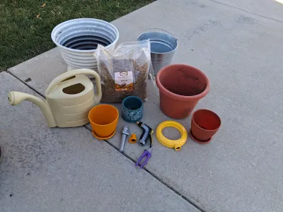 Sale Photo Thumbnail #103: ASSORTED GARDENING SUPPLIES INCLUDING A BAG OF ADAMAN DRIED BSF LARVAE, PLASTIC AND CERAMIC PLANTERS, GALVANIZED BUCKET, WATERING CAN, HOSE NOZZLES, SPRINKLER RING, PRUNERS AND MORE. ITEMS SHOW LIGHT SIGNS OF USE.