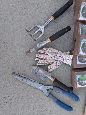 Sale Photo Thumbnail #100: Assorted gardening collection including green plastic watering can, hand trowels, rake tool, shears, floral garden gloves, pots, large storage tote container, coconut coir peat bricks, and boxed solar powered fountain pumps.