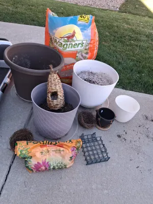 Sale Photo Thumbnail #112: Assorted lawn and garden supply lot including WAGNER'S Songbird Supreme Wild Bird Food, potting mix, multiple plastic and ceramic planters/pots, woven decorative bird roosts/nests, and a suet cage feeder. Items show signs of previous outdoor use and soil 