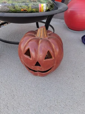 Sale Photo Thumbnail #120: Metal fire pit with mesh spark screen lid and interior grate, American Home by Yankee Candle Fresh Balsam Fir firelog (4.5 lb), ceramic jack-o'-lantern decor, and wood log.