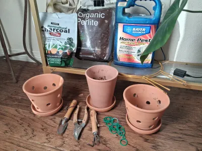 Sale Photo Thumbnail #405: Assorted gardening and plant care supplies including terracotta pots with saucers, hand tools (trowel, pruners, rake), HARRIS Horticultural Charcoal, Organic Perlite, BAYER ADVANCED Home Pest spray, and plant ties.