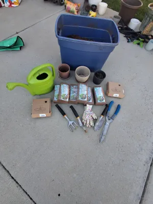 Sale Photo Thumbnail #95: Assorted gardening collection including green plastic watering can, hand trowels, rake tool, shears, floral garden gloves, pots, large storage tote container, coconut coir peat bricks, and boxed solar powered fountain pumps.